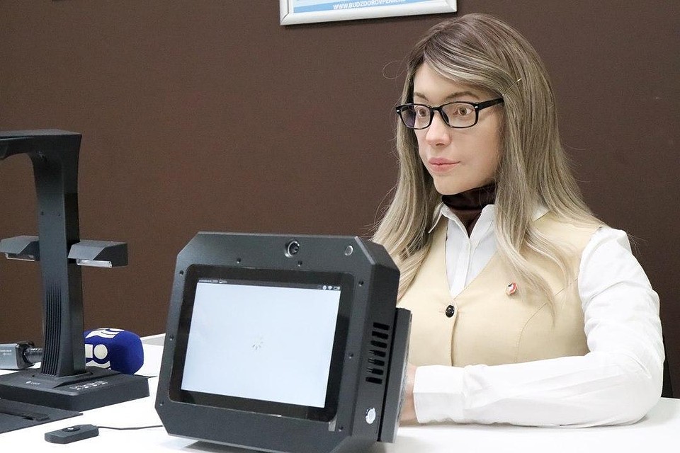 Нового сотрудника приняли на работу в пермский многофункциональный центр «Мои Документы». Это девушка-робот, созданная компанией Promobot. В отличие от обычных Промоботов этот робот очень похож на обычного человека. Он копирует эмоции человека: может двигать глазами, бровями, губами и другими «мышцами» лица, общаться и отвечать на вопросы посетителей МФЦ. Ее внешность была разработана с помощью искусственного интеллекта, который проанализировал внешность нескольких тысяч российских женщин и создал обобщенный образ: девушка с русыми волосами и карими глазами. Специально для нее в МФЦ создали новое рабочее место. Оно практически ничем не отличается от 65 остальных мест для операторов. И получить услугу от робота пермяки смогут практически так же, как от обычного человека. Только быстрее.